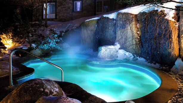 A hot spring with a stone wall and a wooden deck. - Le Westin Tremblant (Mont-Tremblant)