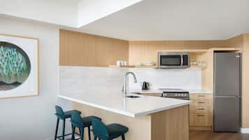 A modern kitchen with a central island, bar stools, a microwave, a refrigerator, and a sink.