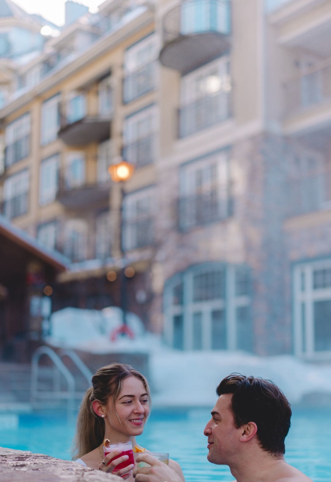 A couple by a pool with a view of a building with balconies.