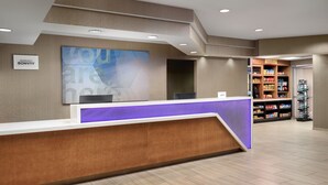 A hotel reception area with a wooden reception desk, a large wall-mounted screen, and a self-service kiosk.