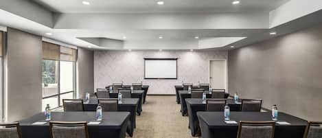 A conference room with a large screen, multiple tables, and chairs, equipped with water bottles.