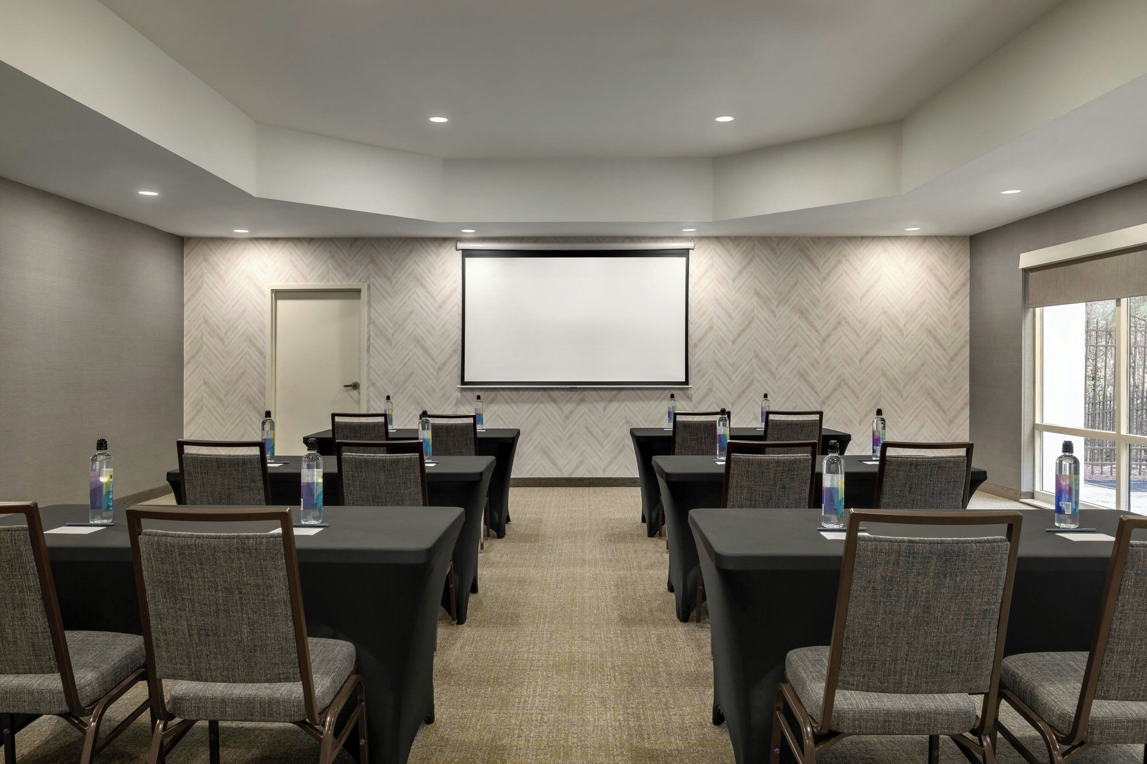Un salón de conferencias con una pantalla grande, varias mesas y sillas.