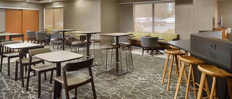 En hotellobby med flera sittgrupper, inklusive bord och stolar, samt en bar med barstolar.