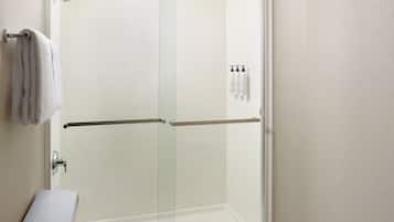 A modern bathroom with a glass shower enclosure, a towel rack, and toiletries on the wall.