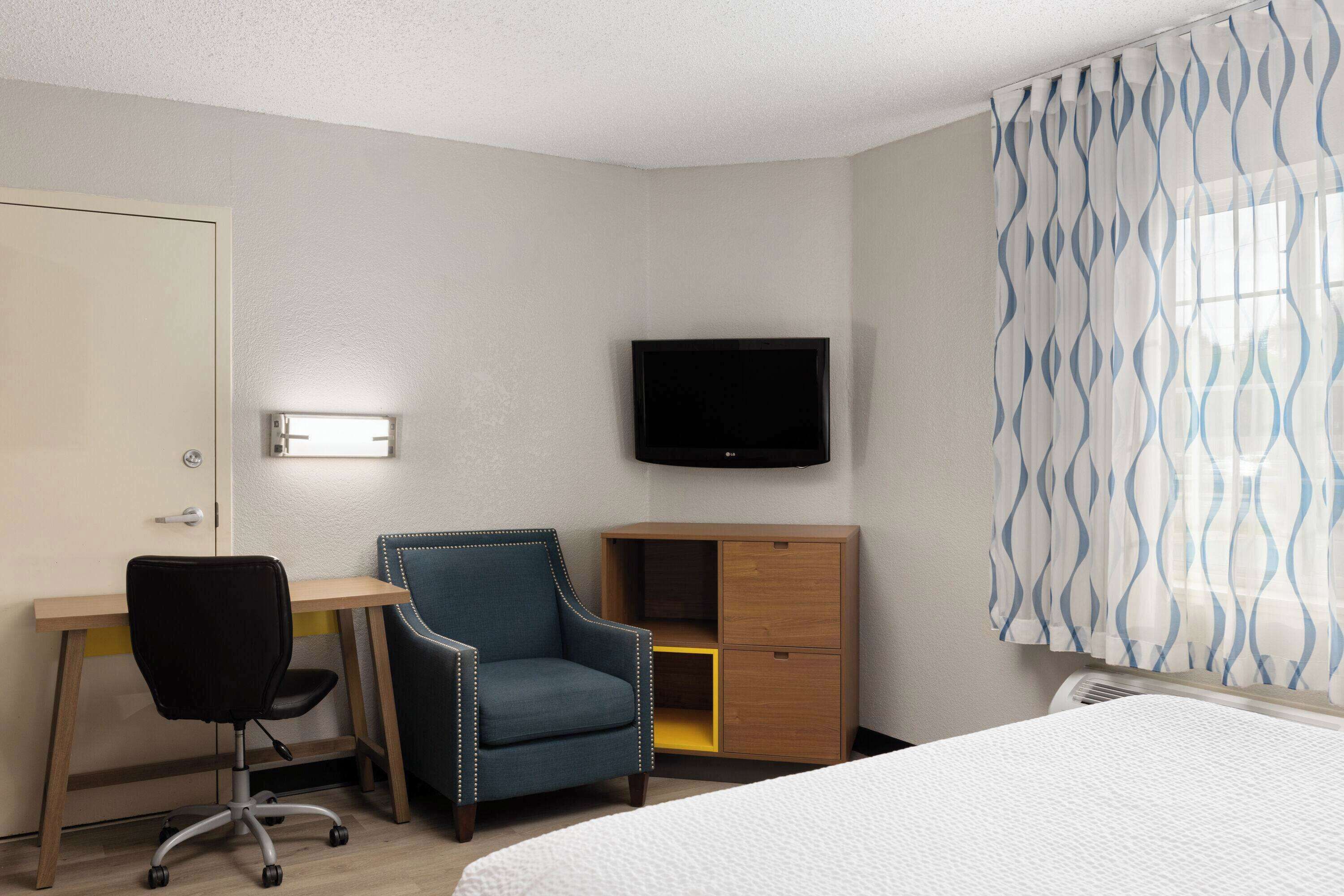 Une chambre d’hôtel comprenant un lit, un bureau avec une chaise, une télévision et une armoire.