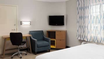 A hotel room with a bed, a desk with a chair, a television, and a wardrobe.