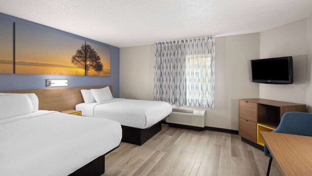 A hotel room with two beds, a desk, a TV, and a window with curtains. - Days Inn & Suites by Wyndham Green Bay WI. (Green Bay)