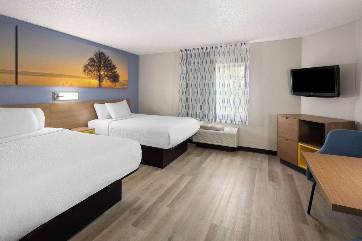 A hotel room with two beds, a desk, a TV, and a window with curtains.