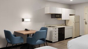 A compact hotel room with a kitchenette, a dining area with two chairs, a bed, and a single door. - Days Inn & Suites by Wyndham Green Bay WI. (Green Bay)