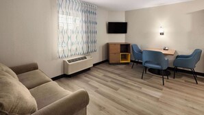 A room with a sofa, a dining table with chairs, a TV mounted on the wall, and a window with curtains. - Days Inn & Suites by Wyndham Green Bay WI. (Green Bay)