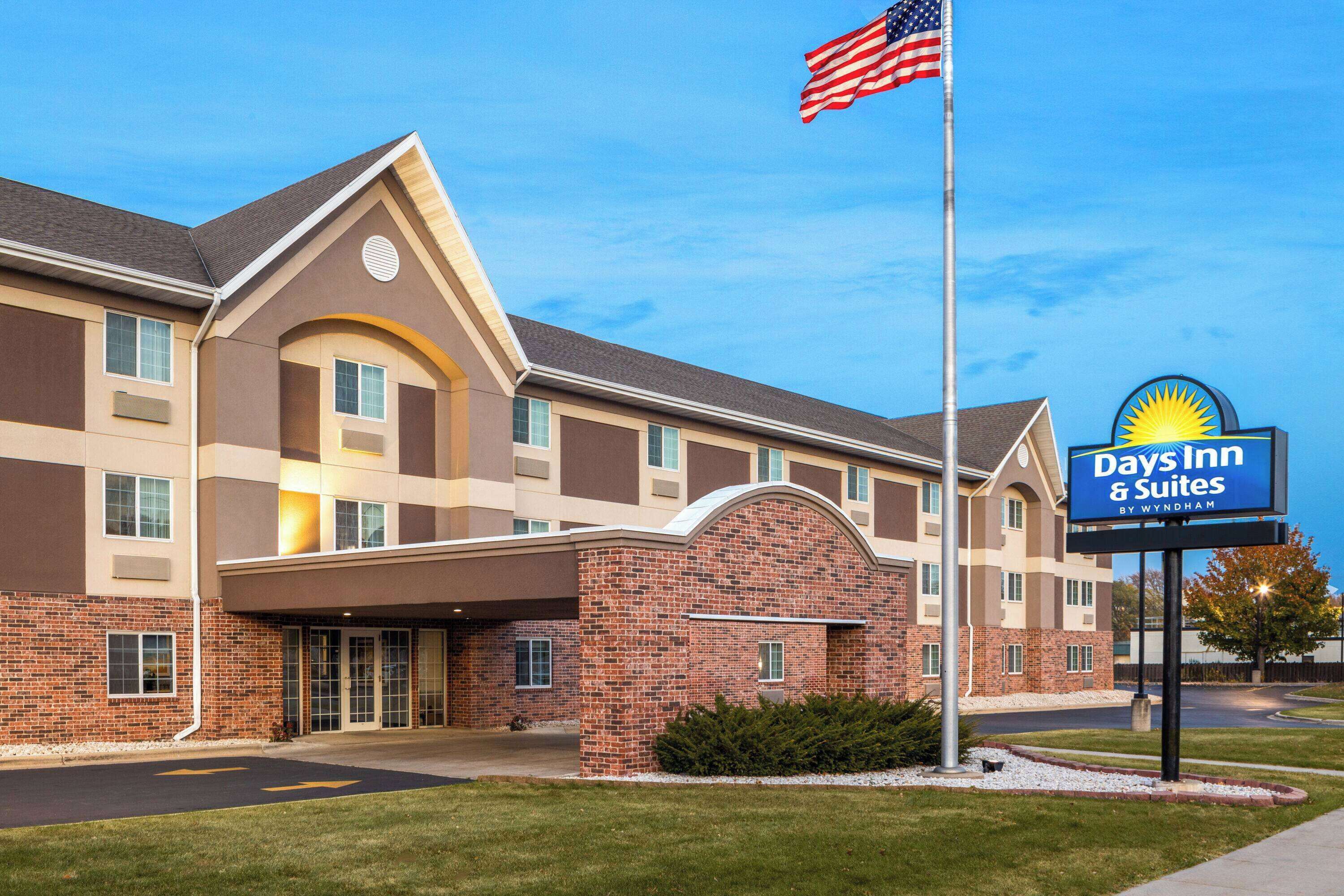 En Days Inn & Suites-byggnad med en fasad av tegel, stora fönster och en amerikansk flagga.