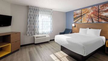 A hotel room with a bed, a TV, a window with patterned curtains, and a painting of trees.