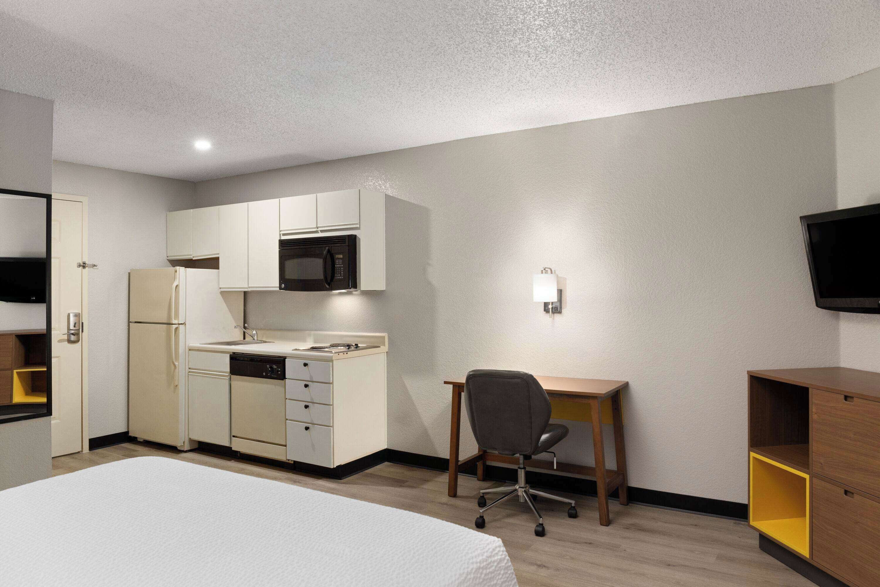 A compact hotel room with a kitchenette, a single bed, a desk, and a TV.