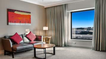 A hotel room with a large window, a sofa, a coffee table, a painting on the wall, and a lamp.