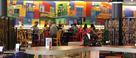 Un restaurante con murales coloridos en las paredes, taburetes de madera en la barra y lámparas colgantes.