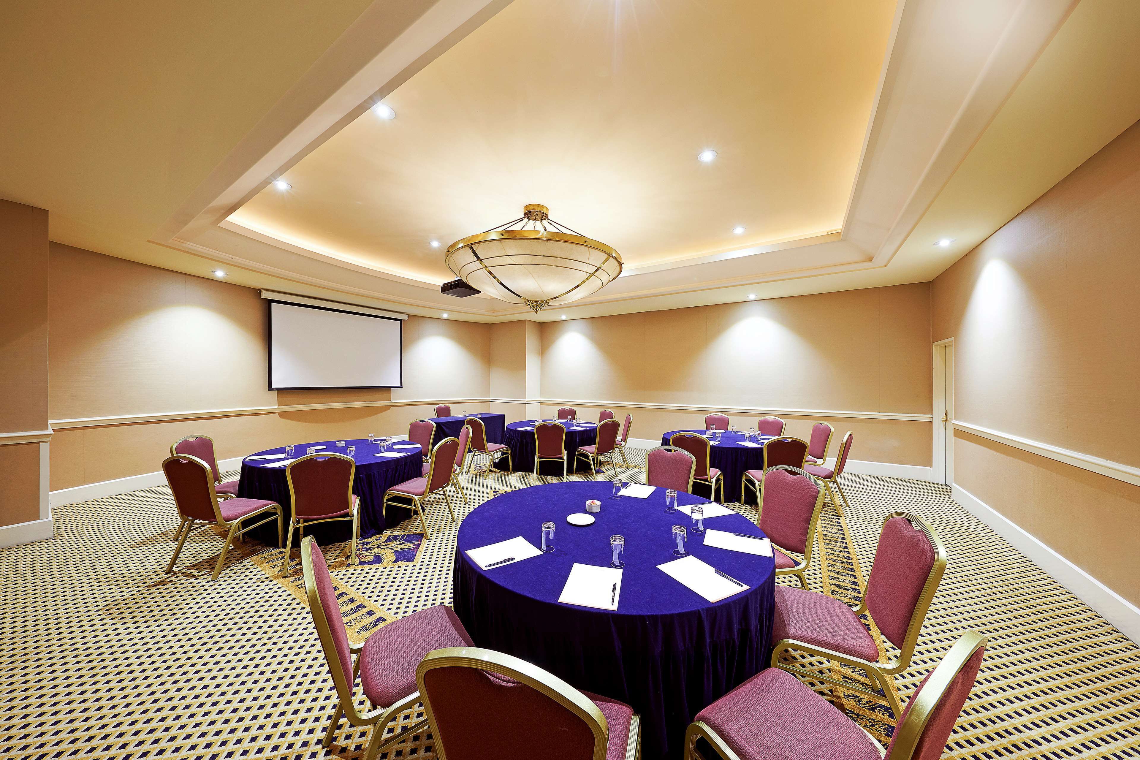 A conference room with round tables, chairs, and a projector screen.