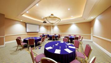 A conference room with round tables, chairs, and a projector screen.