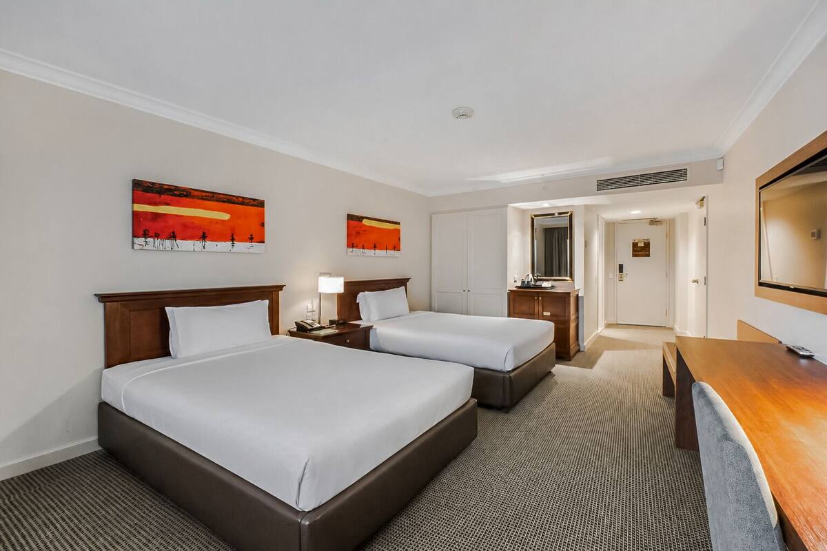 A hotel room with two beds, a desk, a mirror, and artwork on the walls.