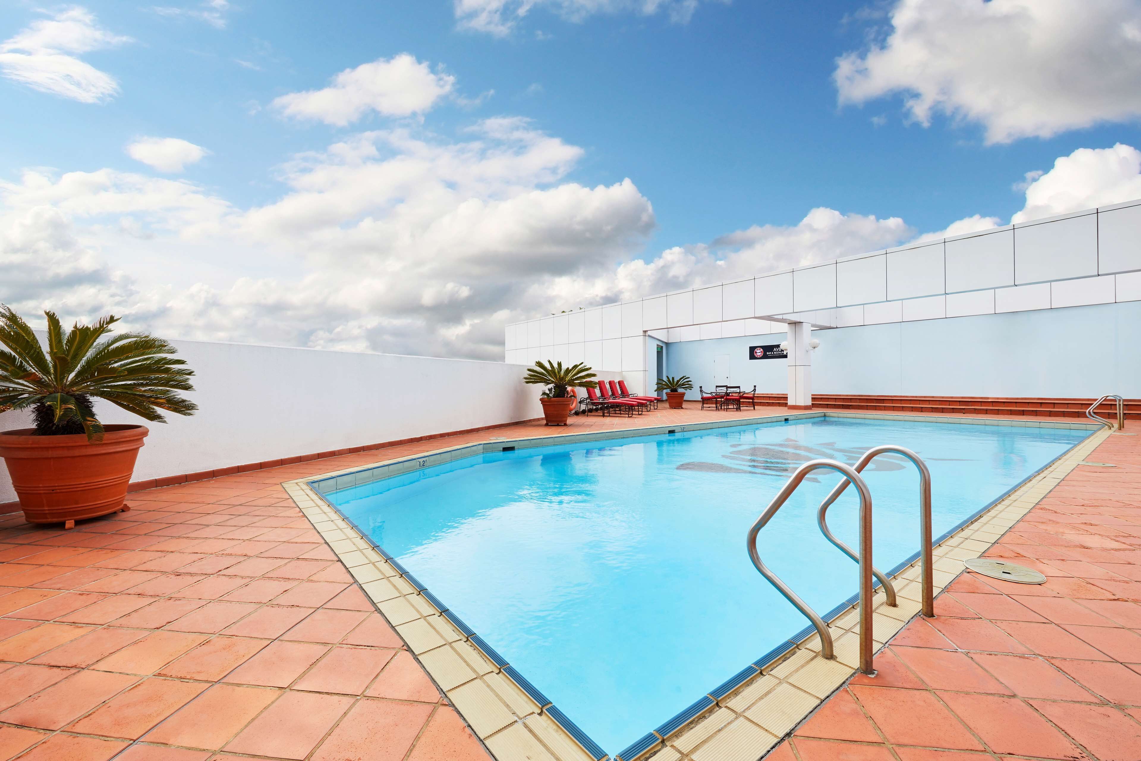 Una piscina sul tetto con cielo azzurro, piante in vasi e sedie rosse.