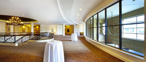 A spacious lobby with a grand chandelier, a balcony with a railing, and large windows offering a view.