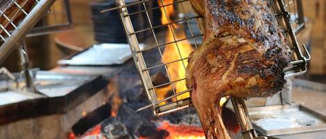 Ein großes, gegrilltes Fleischstück an einem Drehspieß über offenem Feuer.