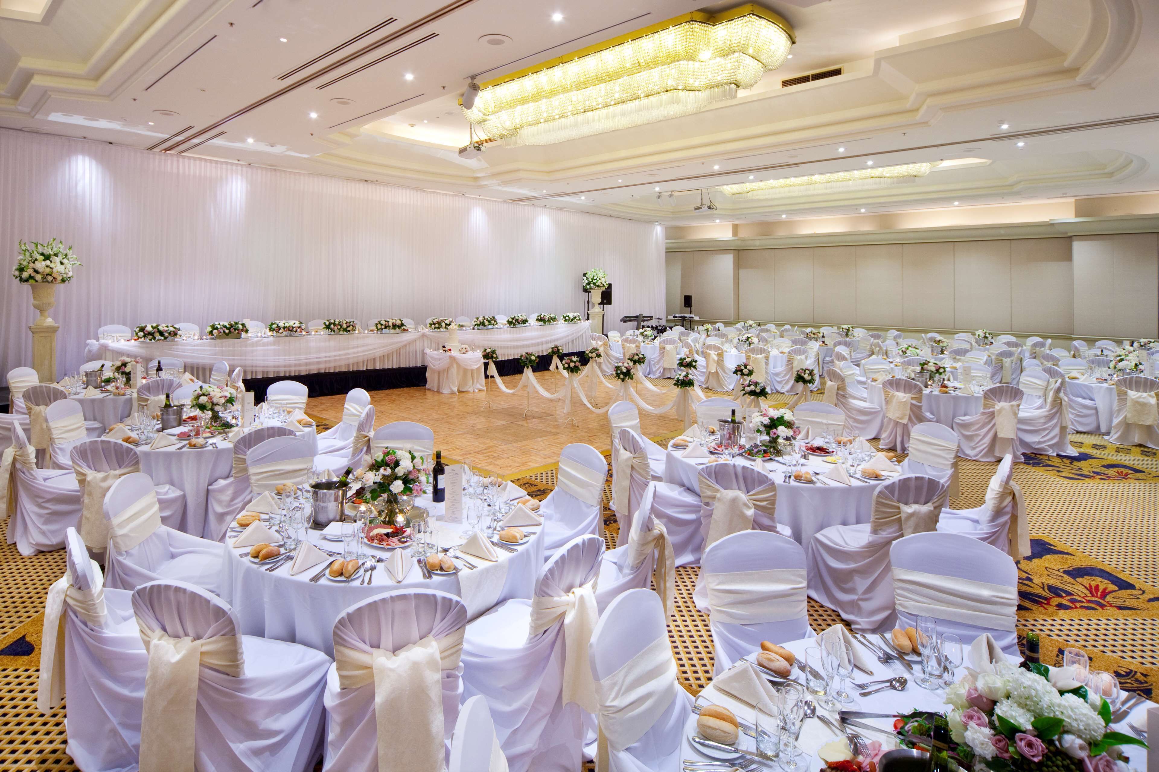 A banquet hall with round tables, white tablecloths, and chairs with white sashes.