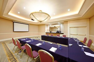 A conference room with a long table, chairs, a projector screen, and a ceiling light fixture.