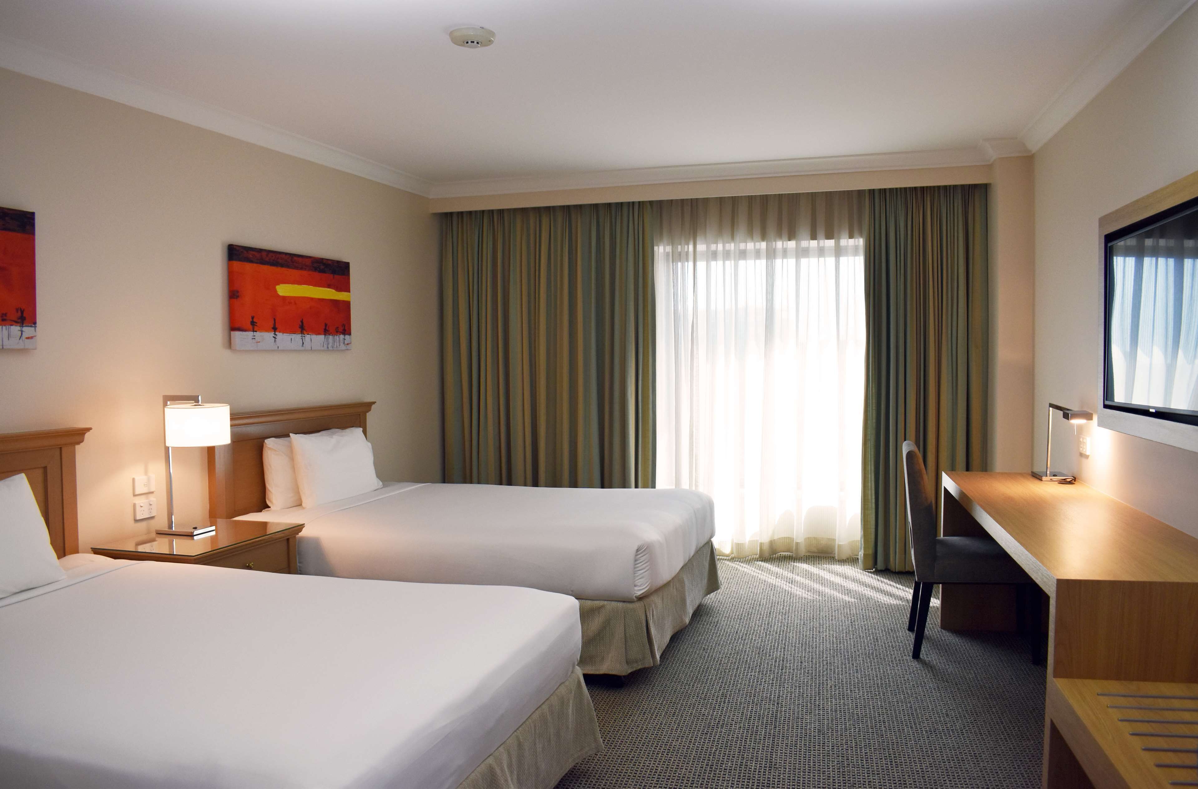 A hotel room with two beds, a desk, a chair, a television, and a window with curtains.