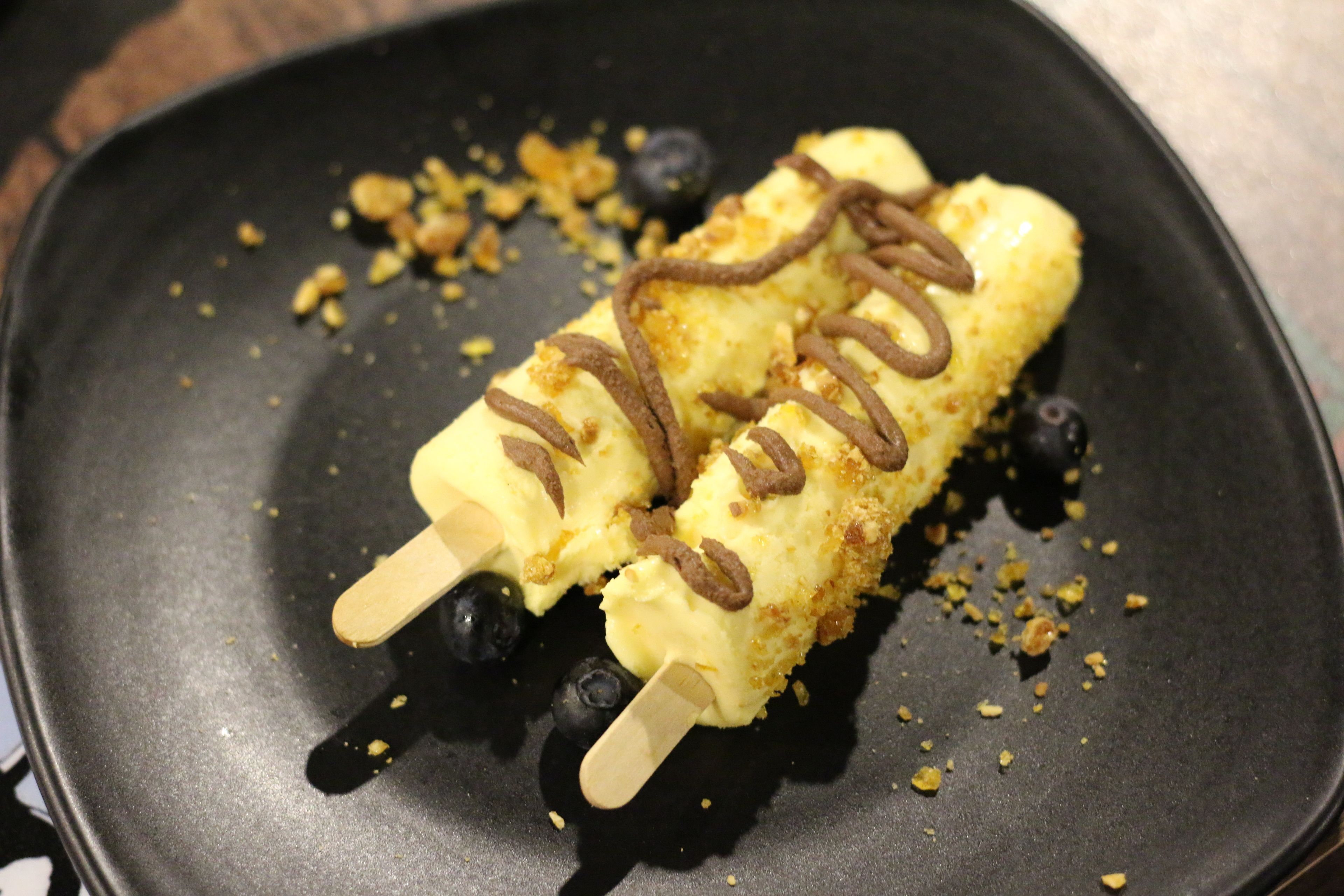 Two ice cream bars on a black plate with crumbs and a wooden stick.