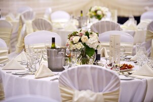 A banquet table set with white tablecloths, glassware, and a centerpiece of flowers.