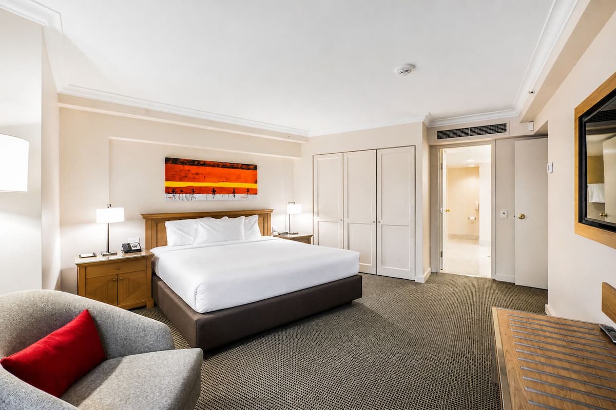 A hotel room with a large bed, two bedside tables, a chair, a painting on the wall, and a wardrobe.