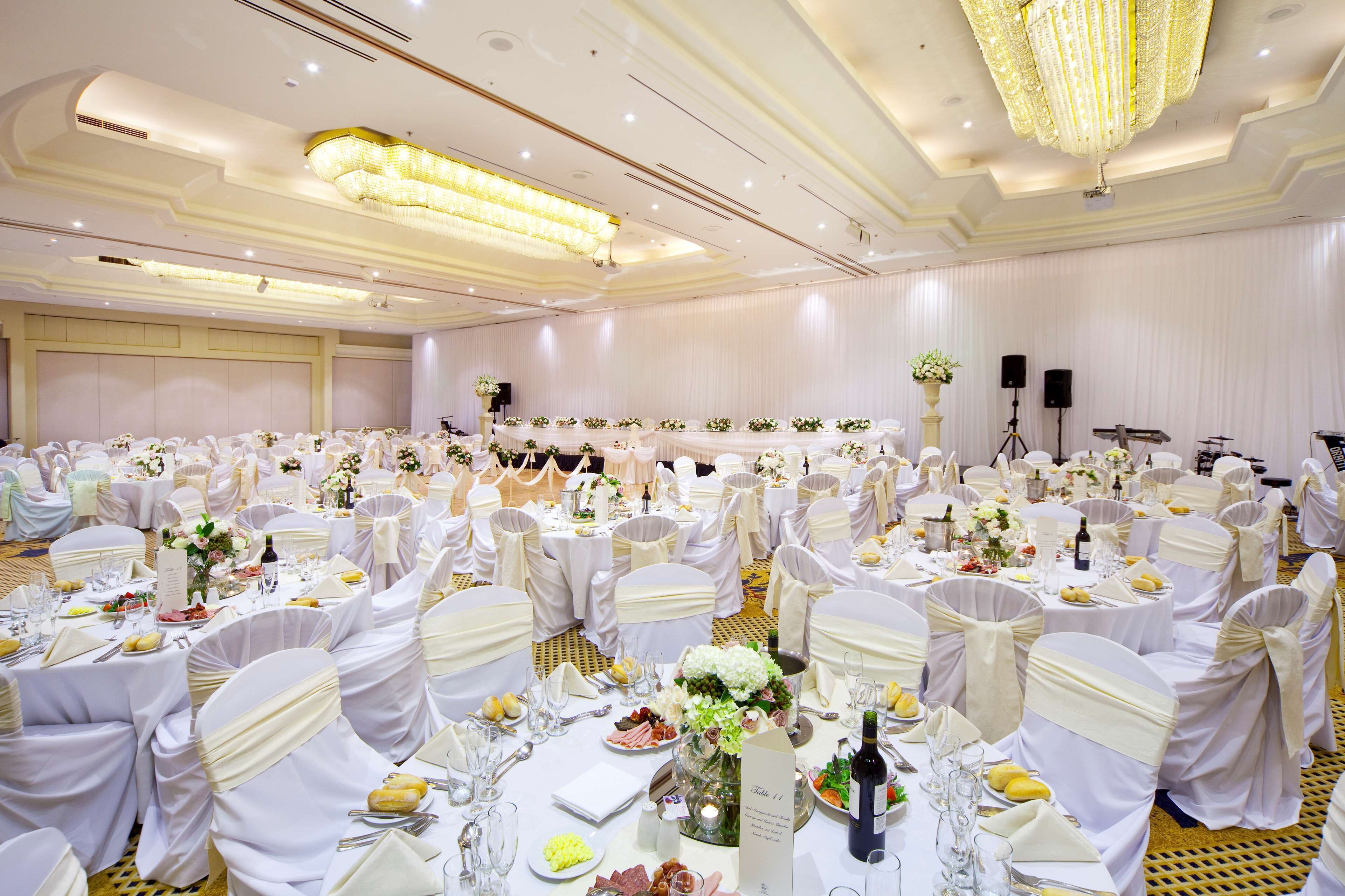 A banquet hall with round tables, white tablecloths, and chairs with white sashes.