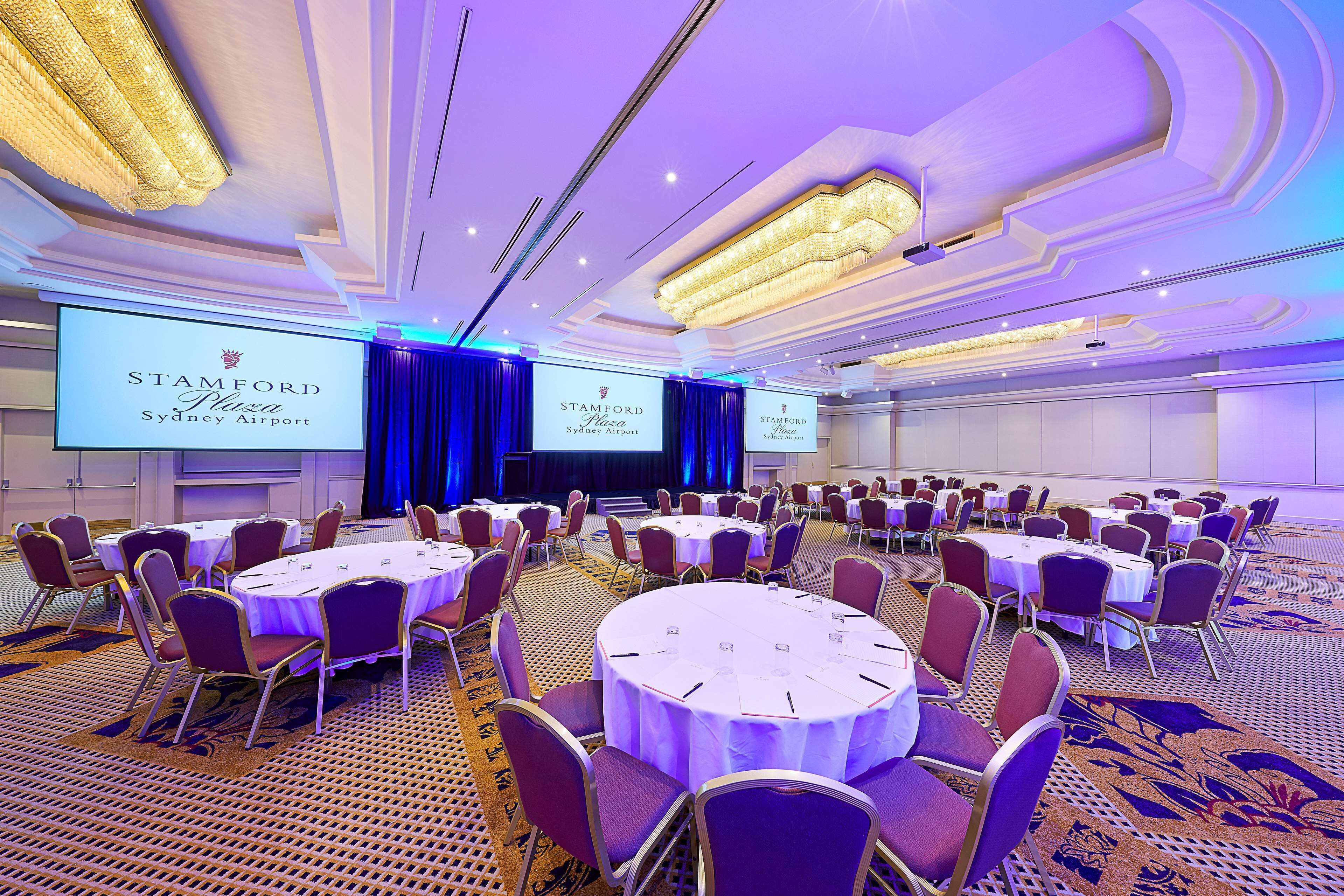 A conference room with round tables, chairs, and a large screen displaying the Stamford Plaza Sydney Airport logo.