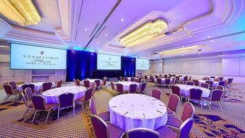 A conference room with round tables, chairs, and a large screen displaying the Stamford Plaza Sydney Airport logo.