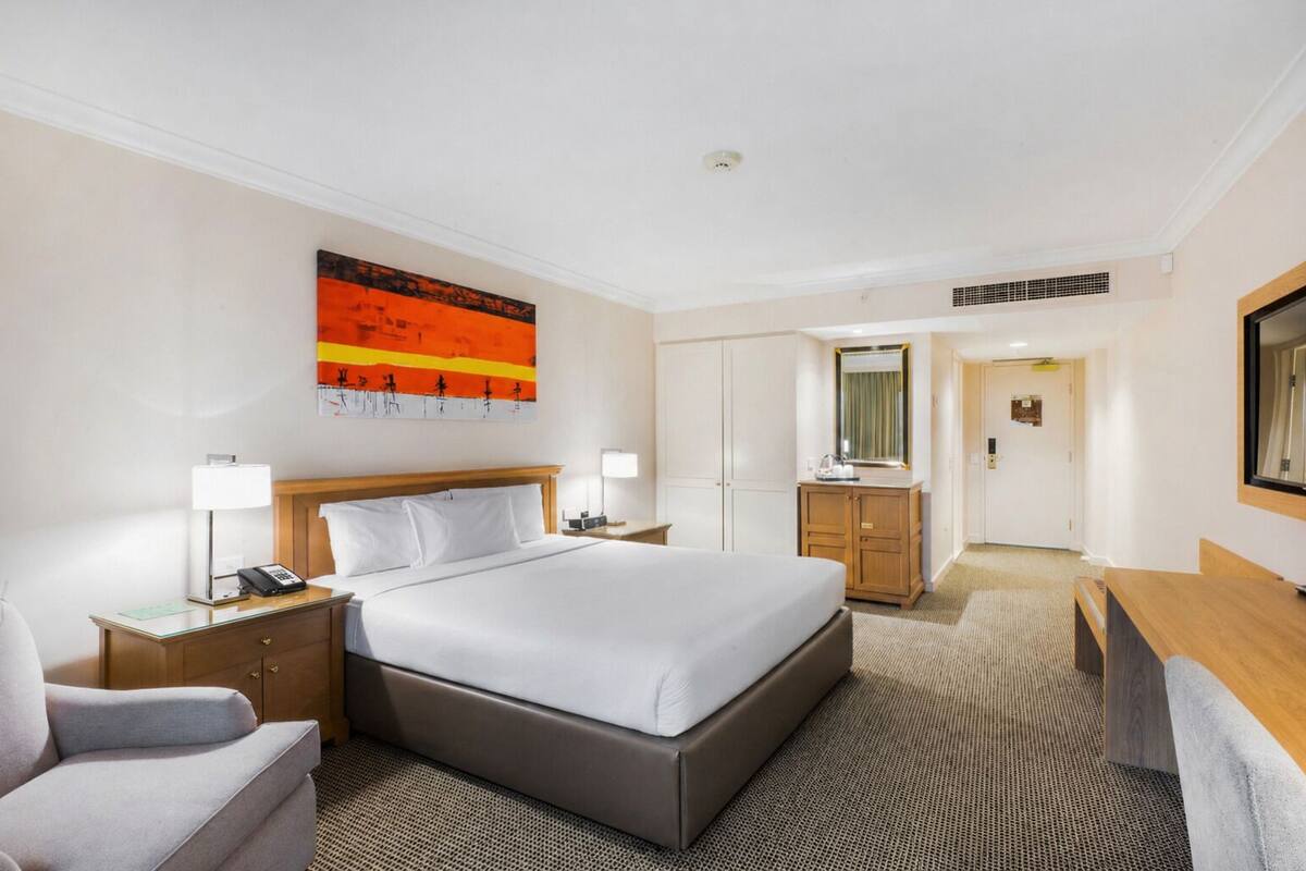 A hotel room with a bed, a desk, a chair, a wardrobe, and a bathroom visible through an open door.