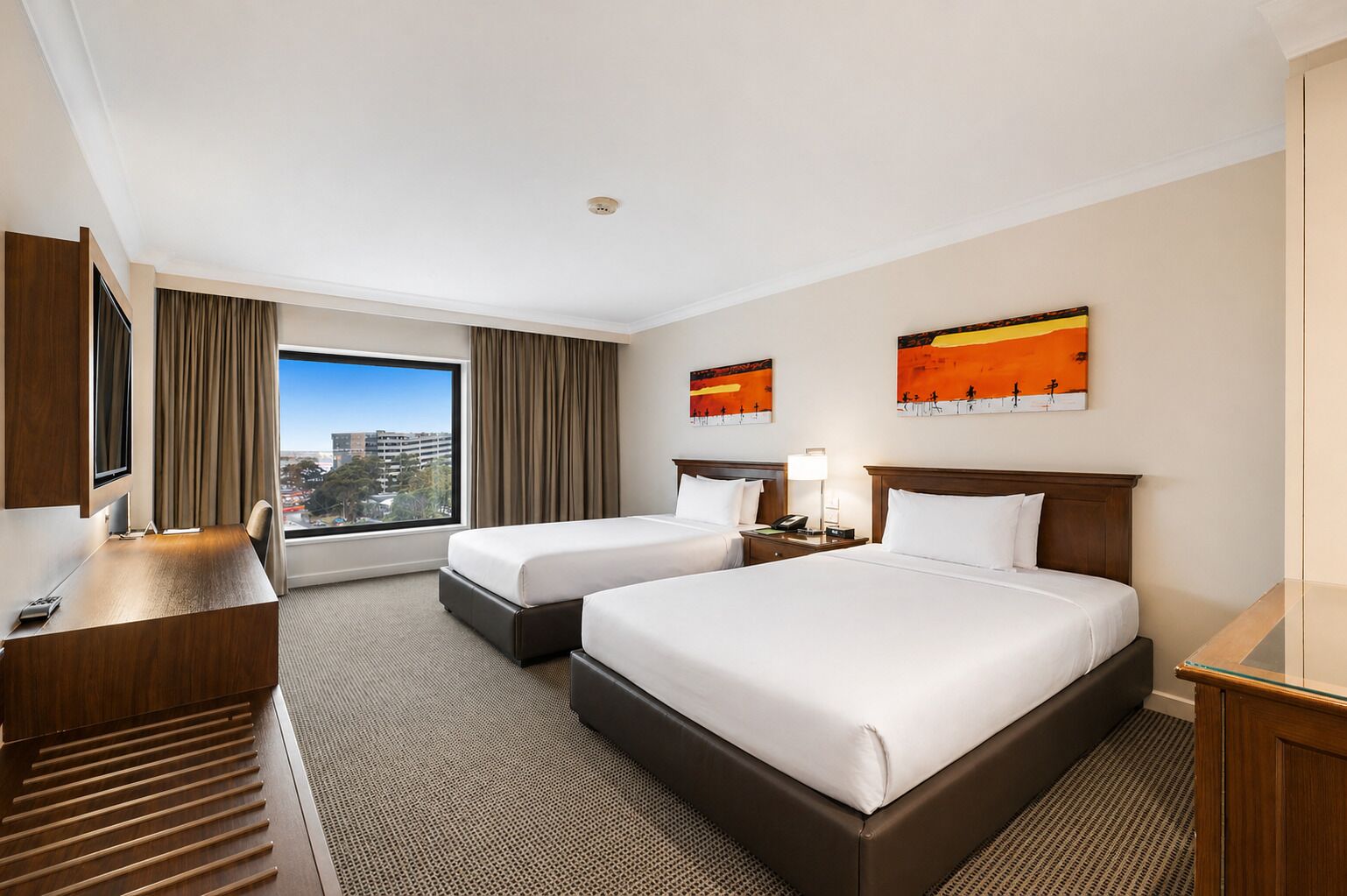Une chambre d’hôtel avec deux lits, un bureau, une télévision et une grande fenêtre donnant sur la ville.