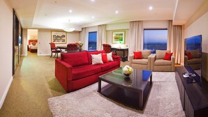 A modern living room with a red sofa, beige sofa, and a coffee table. There is a TV on the right and a dining area in the background. - Stamford Plaza Sydney Airport Hotel & Conference Centre (Sydney)
