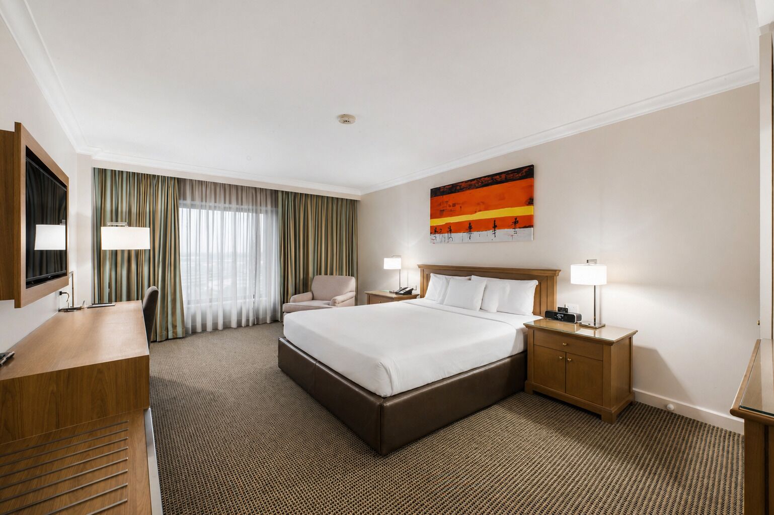 A hotel room with a bed, desk, chair, and a painting on the wall.