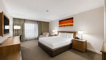 A hotel room with a bed, desk, chair, and a painting on the wall.