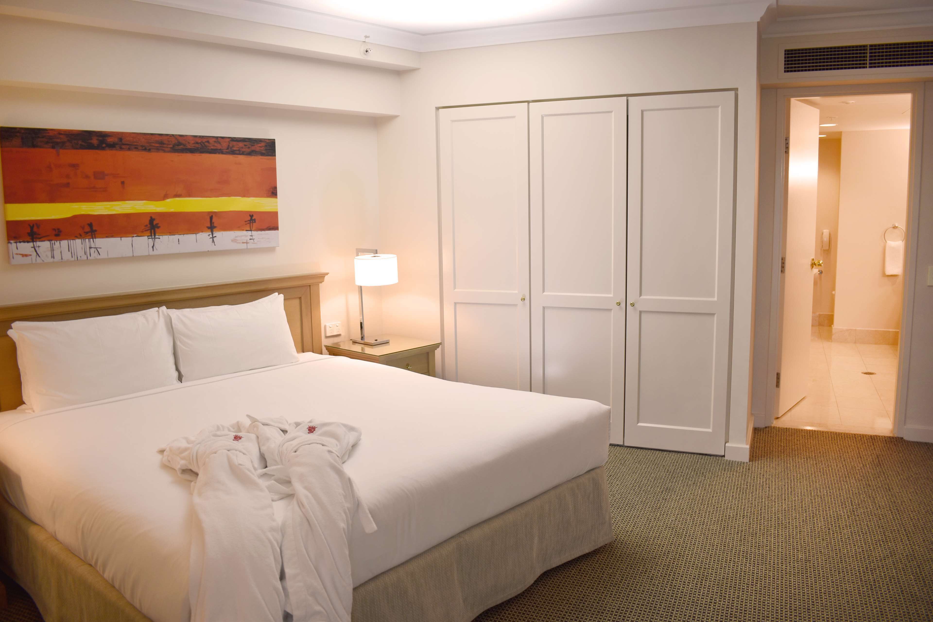 Habitación de hotel con cama, mesita de noche, lámpara, armario y un cuadro en la pared.