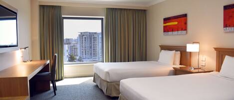 A hotel room with two beds, a desk, a chair, a TV, and a window with curtains.