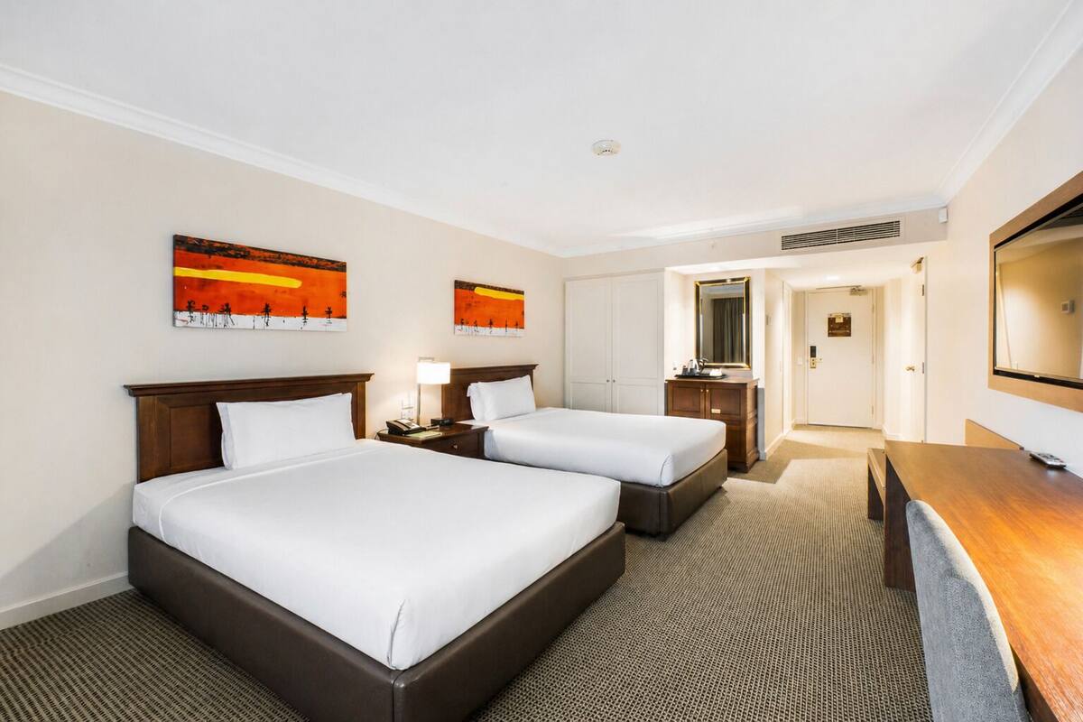 A hotel room with two beds, a desk, a mirror, and artwork on the walls.