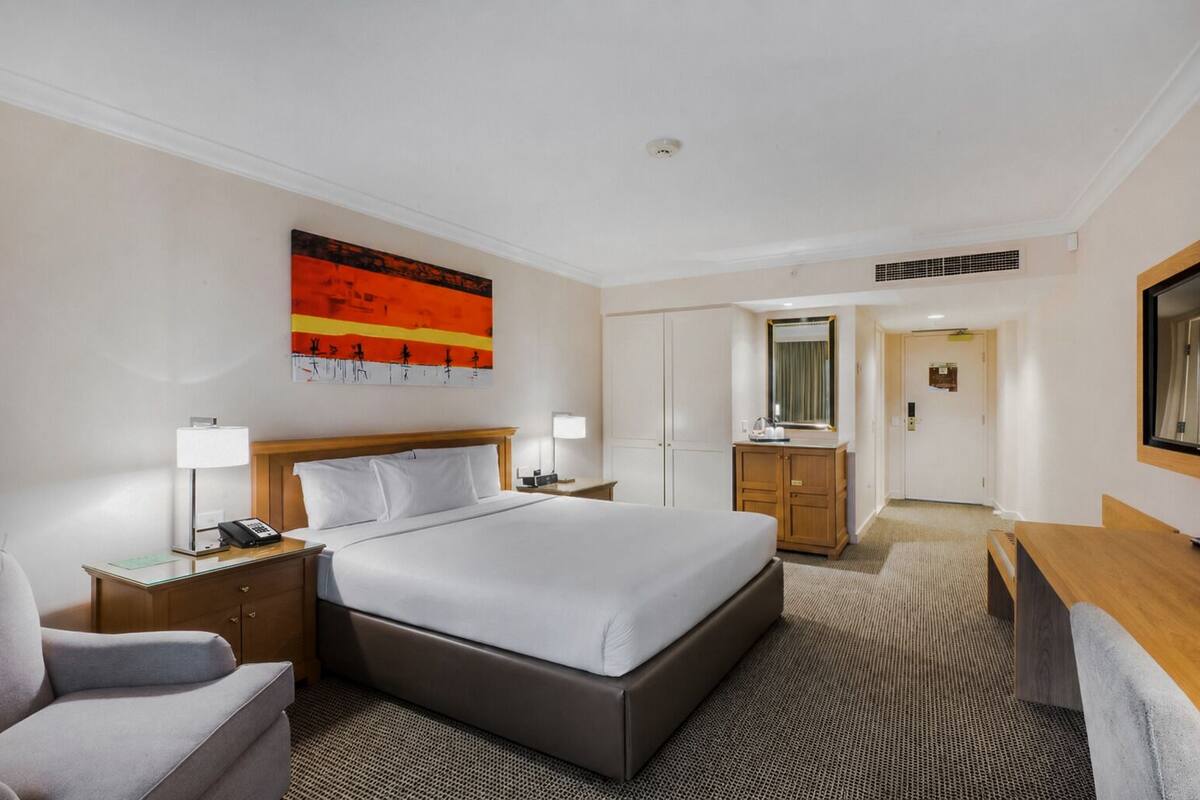 A hotel room with a large bed, a desk, a chair, a wardrobe, and a bathroom visible through an open door.