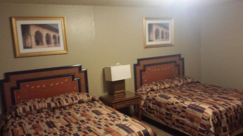 A hotel room with two beds, a nightstand, a lamp, and two framed pictures on the wall.