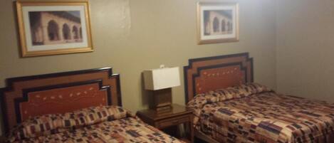 A hotel room with two beds, a nightstand, a lamp, and two framed pictures on the wall.