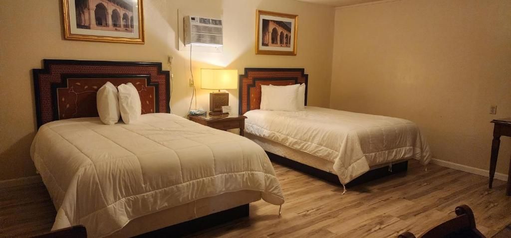 A hotel room with two beds, a wooden floor, and a wall-mounted air conditioning unit.