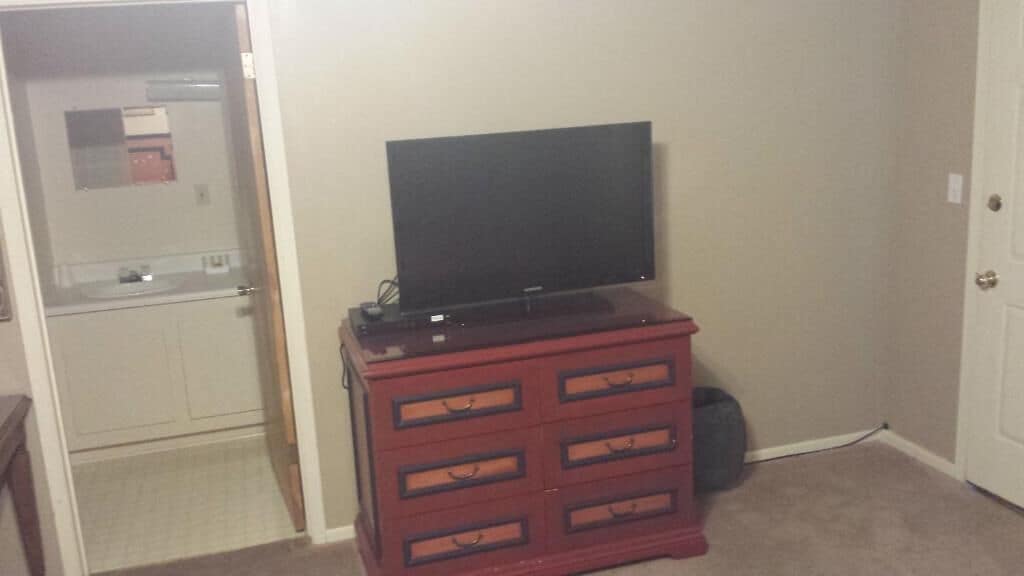 A room with a television on a wooden dresser, a door, and a white wall.
