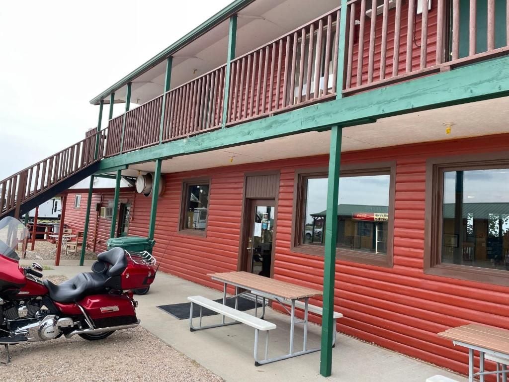 A red building with a balcony, a motorcycle, and a picnic table.