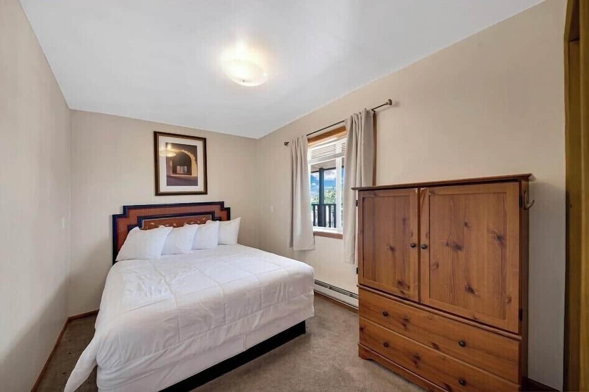 Quarto com cama, guarda-roupa de madeira, quadro na parede e janela com cortinas.