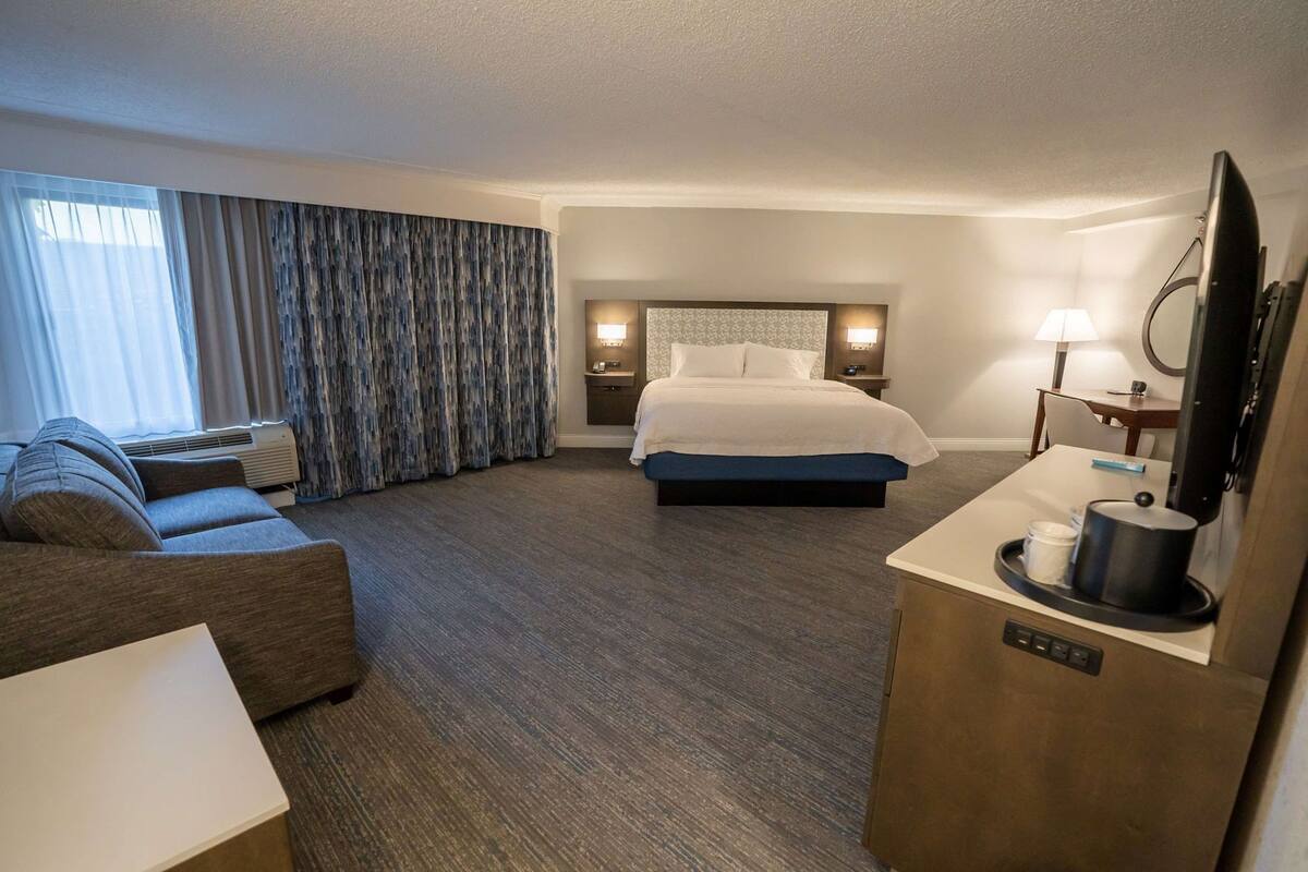 A hotel room with a bed, a sofa, a desk with a TV, and a lamp.